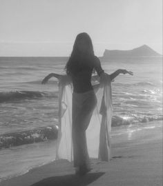 a woman standing on top of a beach next to the ocean holding a sheer curtain