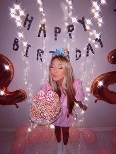 a woman holding a birthday cake in front of balloons