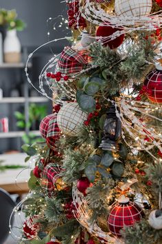 the christmas tree is decorated with red and white balls, greenery, and plaid ribbon