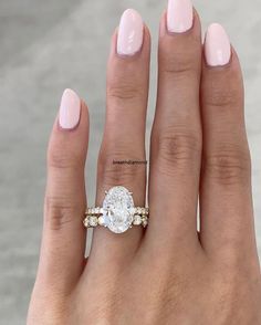 a woman's hand with a pink manicured nail polish and an oval shaped diamond ring