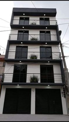 an apartment building with multiple balconies and plants on the top floor, along with two garage doors