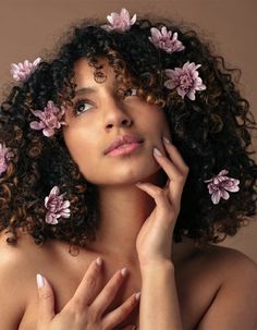 a woman with curly hair and pink flowers in her hair is posing for the camera