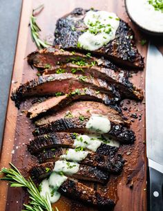 grilled steak with sour cream sauce and herbs on a cutting board next to a knife