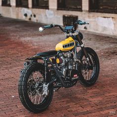 a yellow and black motorcycle is parked on the brick road in front of a building