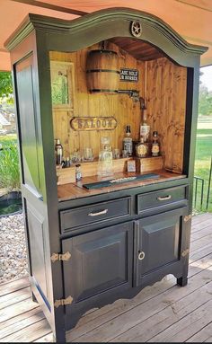 an old fashioned bar is built into the side of a wooden deck with lots of bottles on it