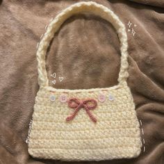 a crocheted purse with a pink bow on the handle sitting on a brown blanket