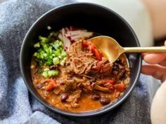 a person is holding a spoon over a bowl of food that includes meat and vegetables