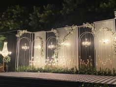 an outdoor wedding setup with chandeliers and greenery on the wall at night