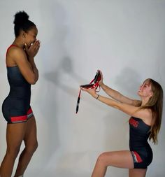 two women in swimsuits are holding shoes and talking on their cell phones while standing against a white wall