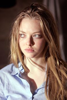 a woman with long blonde hair wearing a blue shirt and looking off to the side