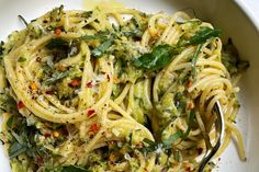 a white bowl filled with pasta and greens on top of a marble table next to a fork