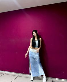 a woman standing against a purple wall with her hands on her hips and looking at the camera