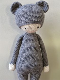 a crocheted gray teddy bear sitting on top of a wooden table next to a white wall