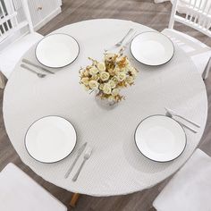 the table is set with white plates and silverware, flowers in a vase on top