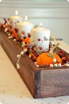 some candles are sitting in a wooden box with berries and pumpkins on the table