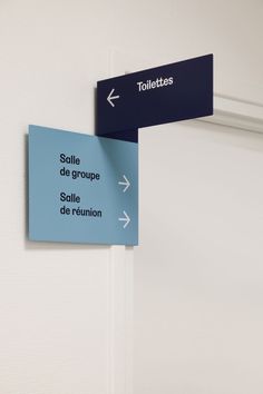 two blue signs hanging from the side of a white wall