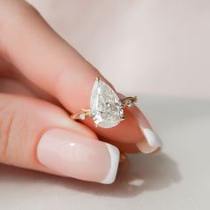 a woman's hand holding an engagement ring with a pear shaped diamond