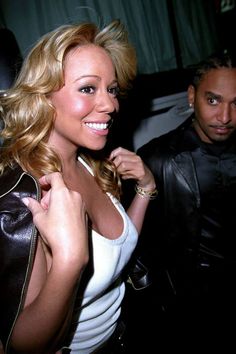 a woman in white shirt and black jacket posing for the camera with a man behind her