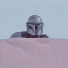 a man in a star wars helmet sitting on top of a pink blanket looking out over the desert