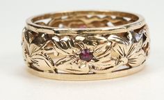 a close up of a gold ring with flowers on the side and a red stone in the middle