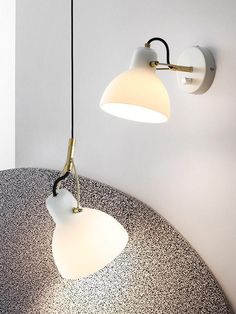 two lights are hanging on the wall next to a round table with a black and white pattern