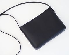 "This simple crossbody bag features black leather with fabric lining and a magnetic closure. Details: -Dimensions: 7\" length (top to bottom), 11\" top width and 9\" bottom width (side to side), 2\" depth, 9\" X 2\" base (bottom) -Shoulder strap is not adjustable. Please select the length. If you are not sure, please select \"other\" and email me your height. -Cotton interior lining (navy) - color can be customized -One internal slip pocket -Magnetic closure Because each bag is made by hand, the Versatile Black Leather Flap Bag, Modern Black Square Flap Bag, Sleek Black Flap Bag For Everyday Use, Black Soft Leather Flap Bag For Office, Minimalist Black Business Shoulder Bag, Sleek Black Leather Flap Bag, Black Soft Leather Rectangular Flap Bag, Sleek Black Shoulder Bag With Adjustable Strap, Black Soft Leather Crossbody Flap Bag