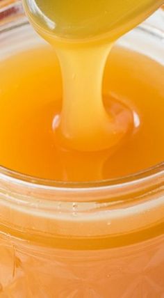 a spoon is pouring honey into a jar