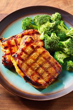 two pieces of meat and broccoli on a blue plate sitting on a wooden table