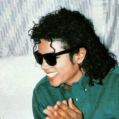 a man wearing sunglasses sitting on top of a white couch with his hands folded in front of him