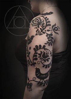 a woman's arm with black and white tattoos on her left arm, in front of a dark background