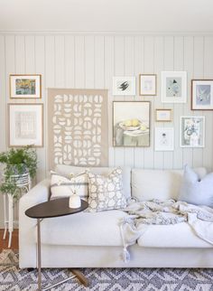 a living room filled with white furniture and pictures on the wall above it's coffee table