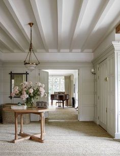 a living room filled with furniture and flowers on top of a wooden table in front of a piano