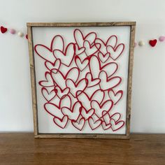 a wooden frame with hearts cut out of it on top of a table next to string lights