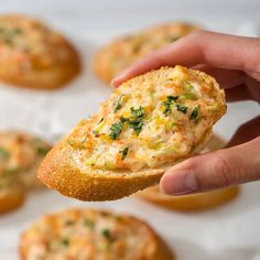 a hand holding up a piece of bread with cheese and herbs on it