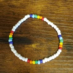 a white beaded bracelet with multicolored beads on a wooden surface, resting on a table