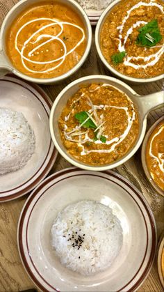 several bowls of different types of food sit on a wooden table, with rice and sauces in them