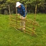 a man leaning over a wooden fence made out of sticks and bamboo poles in the grass