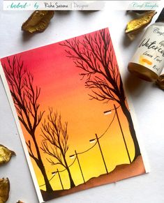 a card with trees and street lights painted on it, next to some wine bottles