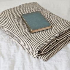 a stack of folded books sitting on top of a bed next to a white comforter