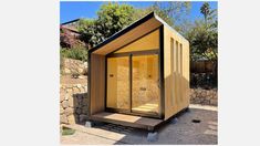 a small wooden structure sitting in the middle of a yard next to a stone wall