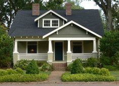 a small gray and white house surrounded by greenery in the front yard with trees on either side