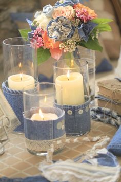 some candles are sitting on a table with blue napkins and flowers in vases