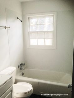 a white toilet sitting next to a bath tub in a bathroom with a window above it