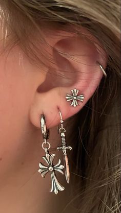 a close up of a person's ear with cross and arrow earrings on it