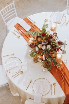 the table is set with an orange and gold runner, candles, and flower centerpieces