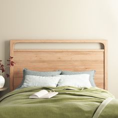 a bed with green linens and pillows in a white walled room, next to a wooden headboard