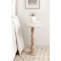 a small white table with a plant on it next to a bed in a room