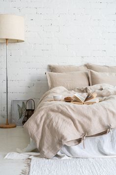 an unmade bed with a book on it in front of a white brick wall