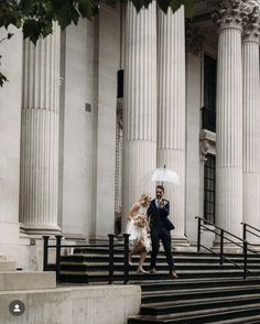 a bride and groom walking down the steps under an umbrella in front of a building