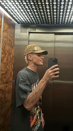 a man taking a selfie with his cell phone in an elevator stall while wearing a hat